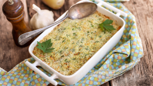 An oven dish with brandade with spoon, a bulb of garlic and pepper shaker