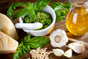 Pesto in a bowl with serving spoon next to herbs and bulb of garlic