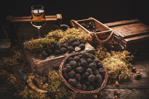 A basket filled with black truffles surrounded by hay, wooden crates and a glass of rose.