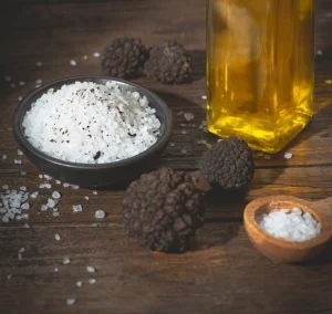 Truffle salt in a black dish beside black truffles on wooden table.
