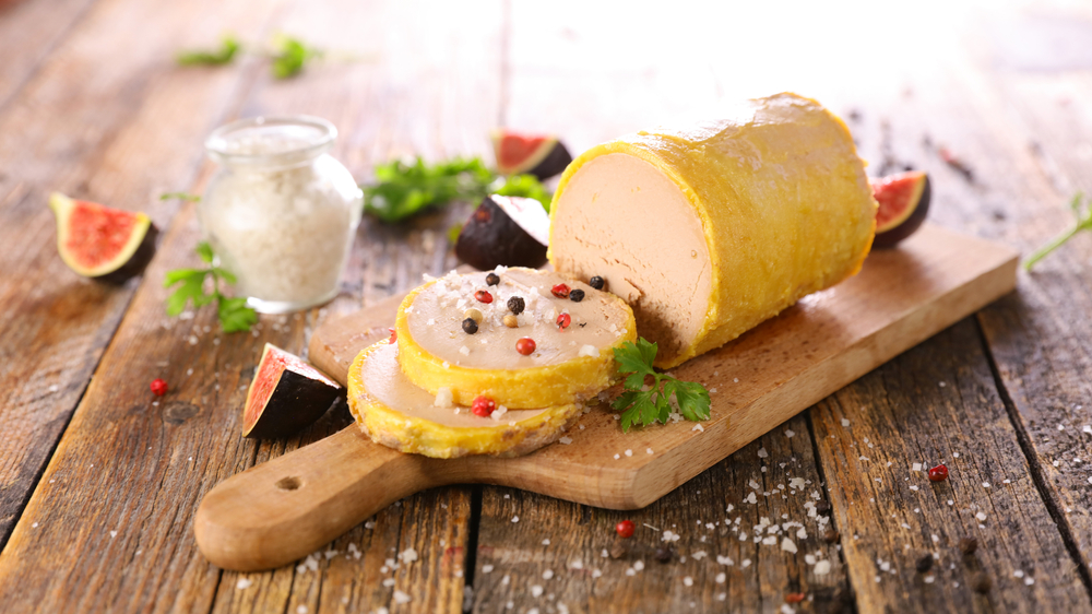 Foie Gras with two slices on a wooden chopping board with figs beside it.