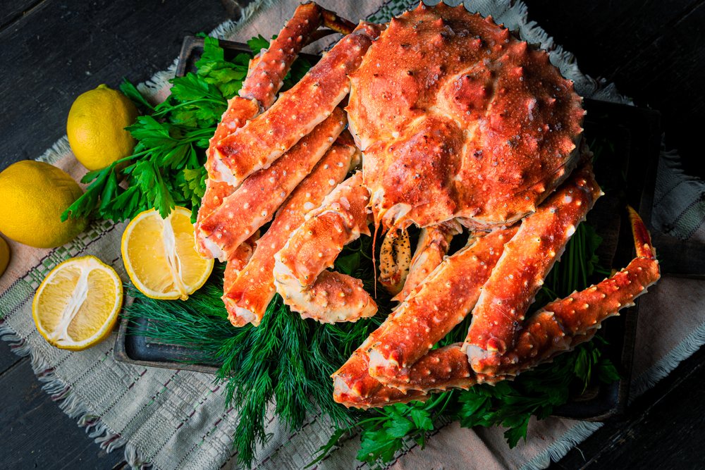 Whole king crab on herbs with lemons beside.