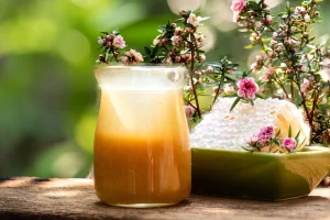 Manuka Honey in jar next to dish with honeycomb and flowers