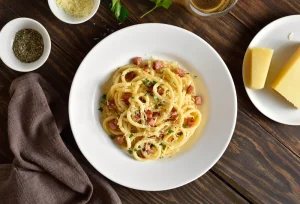 A white bowl of carbonara next to a plate with cheese on it.