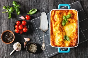 Lasagna in a dish beside slicer and tomatoes.
